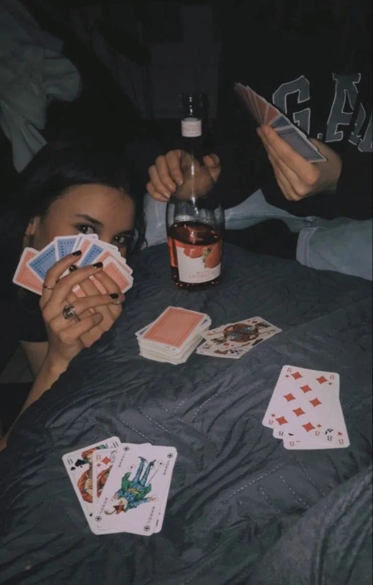 A late hand of cards over a quilted bed, bottle of rosé in the middle of the deal.