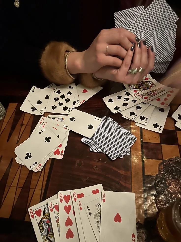 A fanned hand of cards held close over a dark wooden table, scattered cards in candlelight.