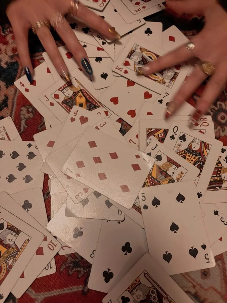 Hands diving into a pile of scattered playing cards on a deep red rug.