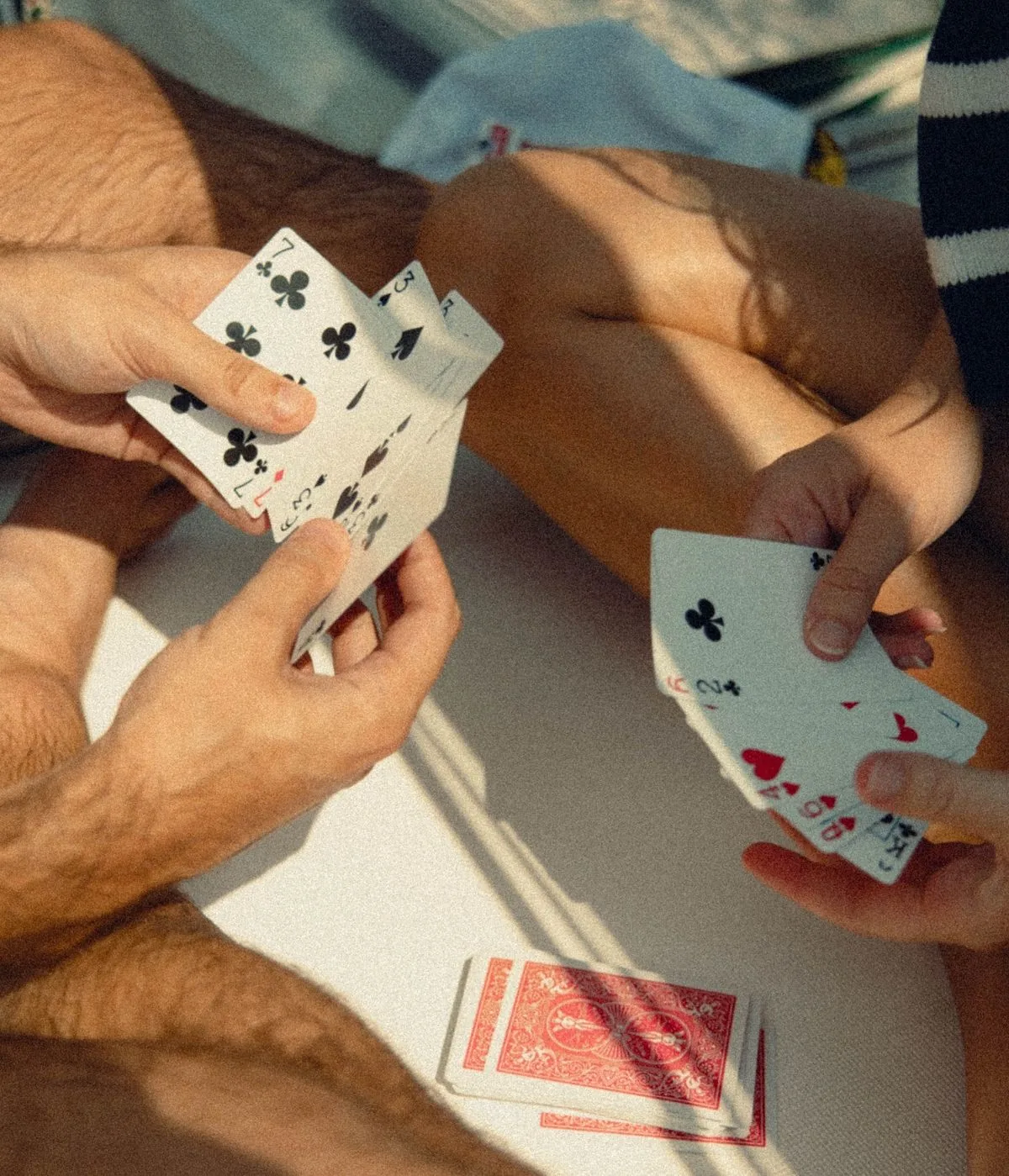Two players holding fanned hands of cards in late-afternoon sun, a deck face down between them.