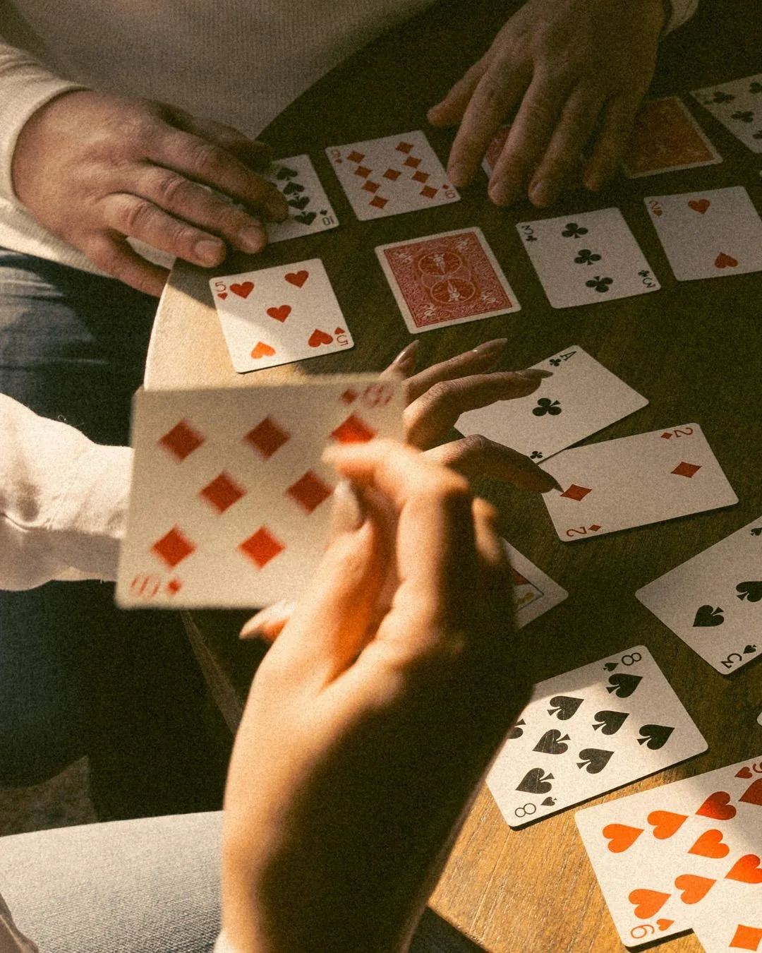 A hand fanning a card over a warmly lit table, others already played around it.