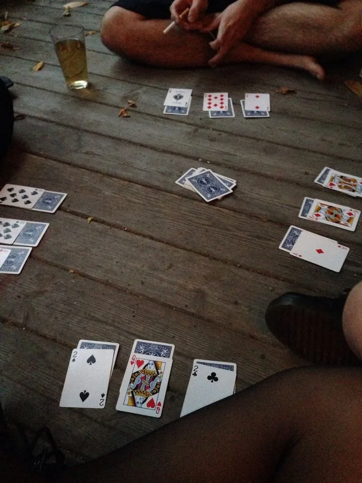 Cards laid out across the weathered boards of a cabin porch, a glass of beer and fallen leaves around them.
