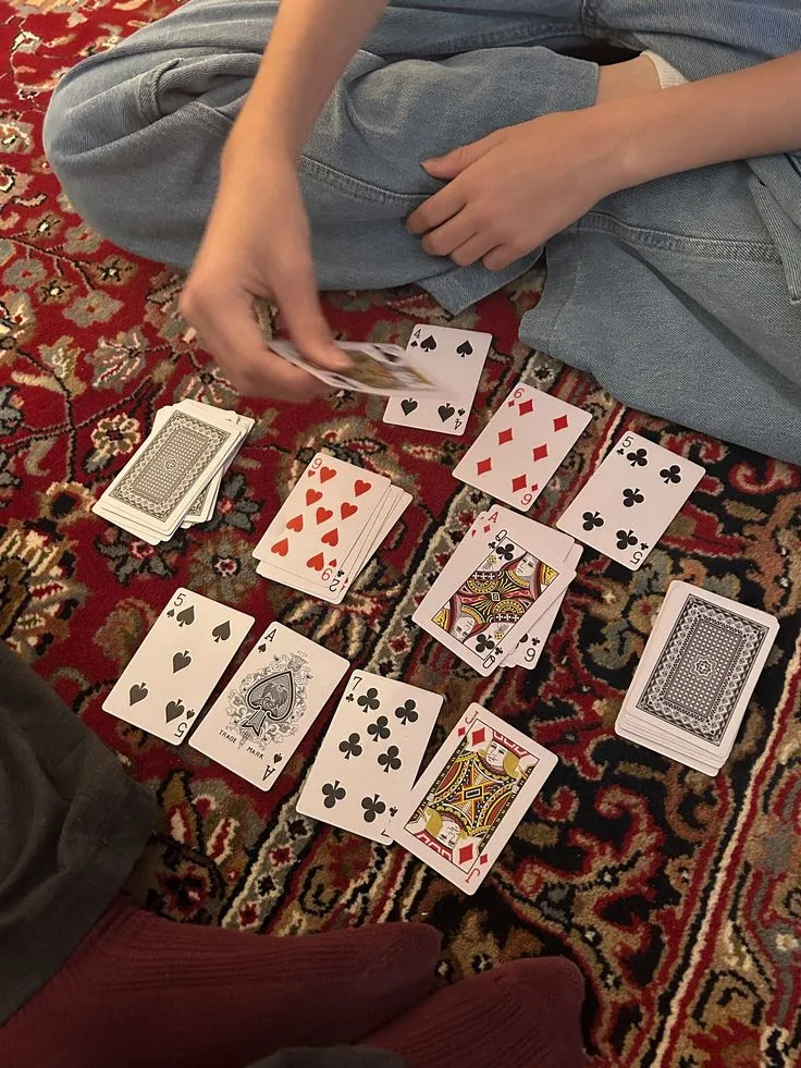 Cards laid out in a row on a red patterned rug, a player cross-legged in jeans mid-deal.