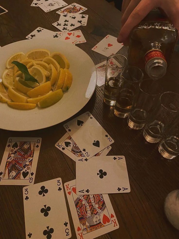 A late table of cards beside a plate of lemons, a tequila bottle, and a row of shot glasses.